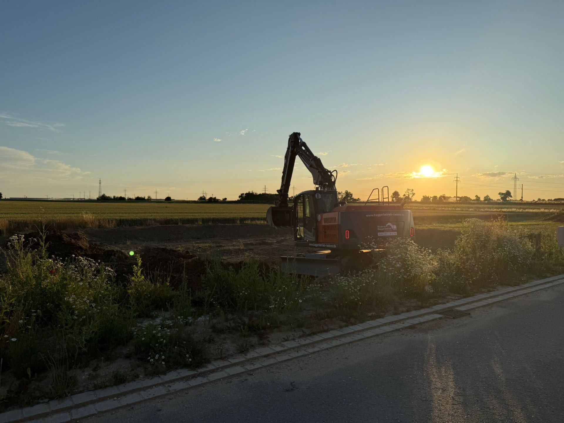 Bagger der Firma Riederer Baggerbetrieb bei Sonnenuntergang im Feld